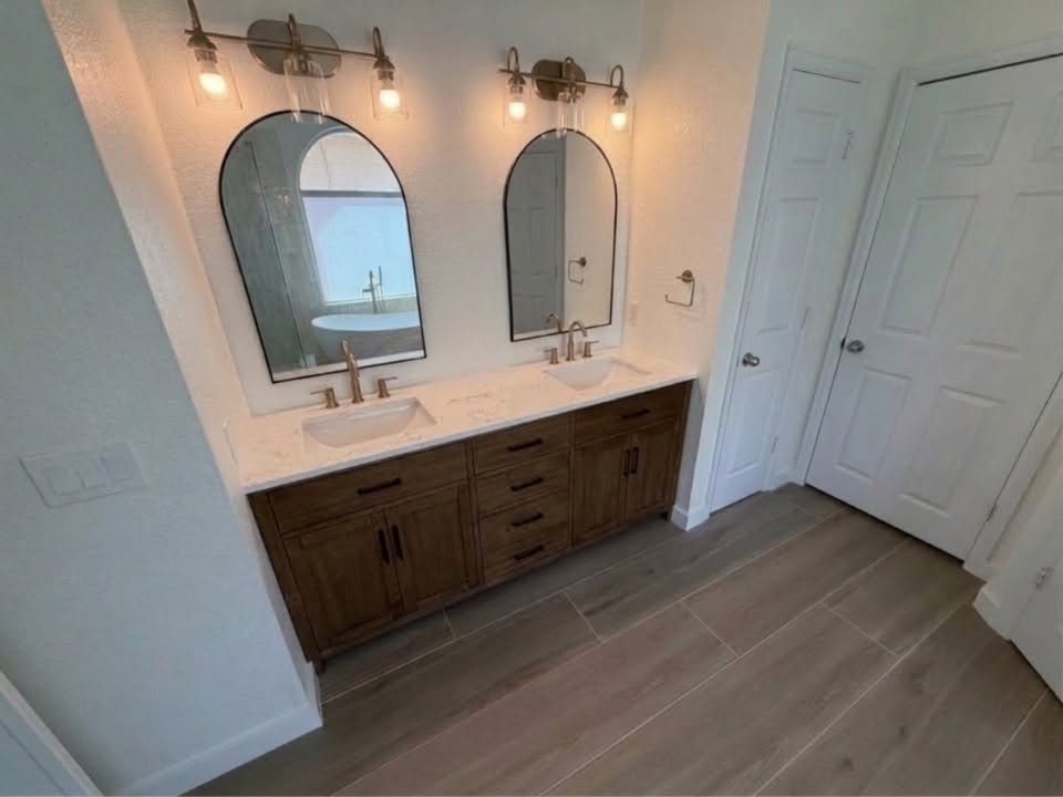 Dark wood double vanity with two arched mirrors and brass sconces