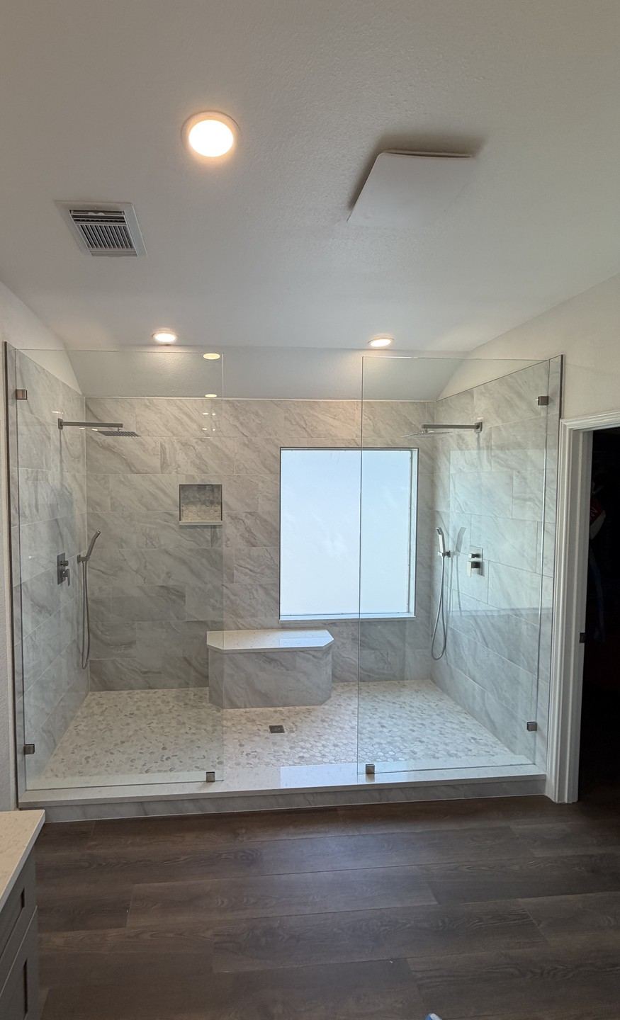 Finished walk-in shower with dual showerheads, a built-in bench and niche, enclosed by two glass panels with no door