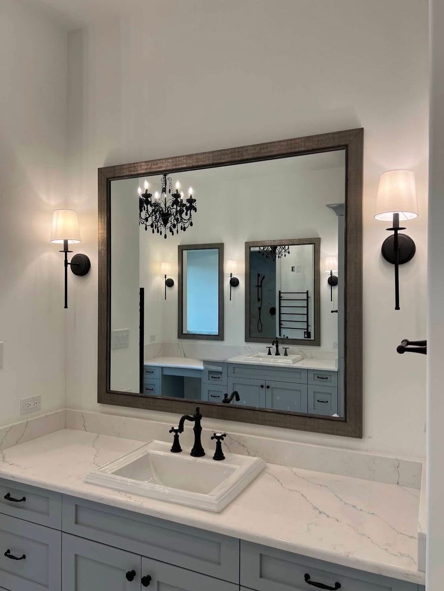 Gray shaker vanity with quartz countertop, a framed mirror, oil-rubbed bronze faucet and black sconces with linen shades