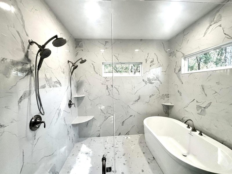 Marble-look wet room with a freestanding tub inside a glass-enclosed shower area and a window